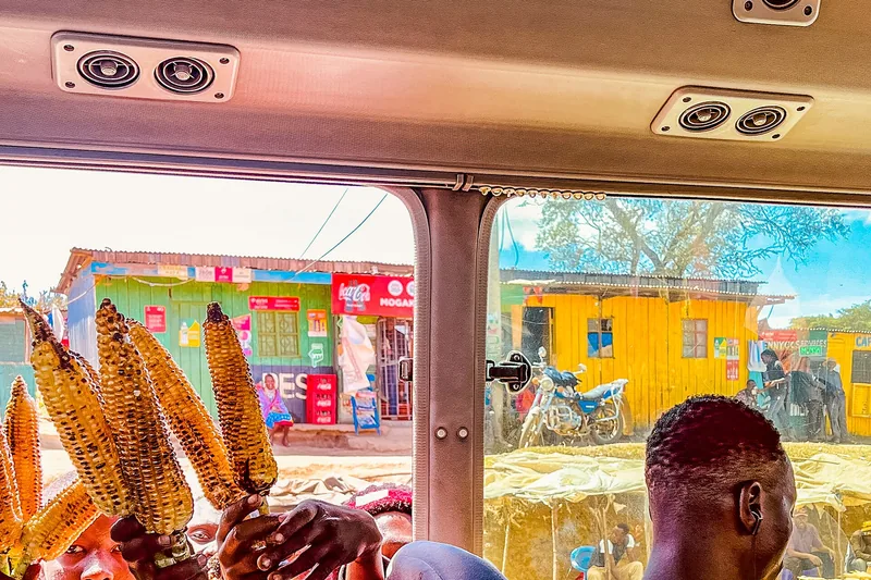 A travel documentary frame from inside a vehicle looking at a colourful roadside market in Kenya