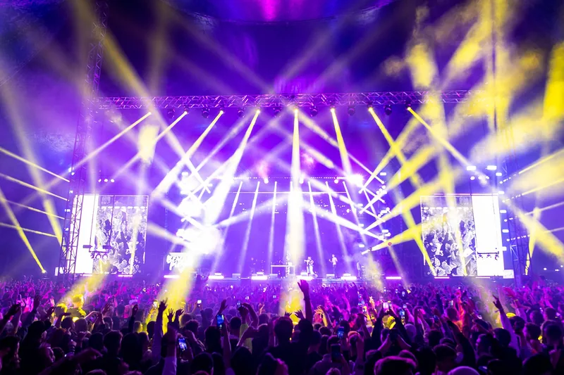A concert crowd under purple and yellow stage lights